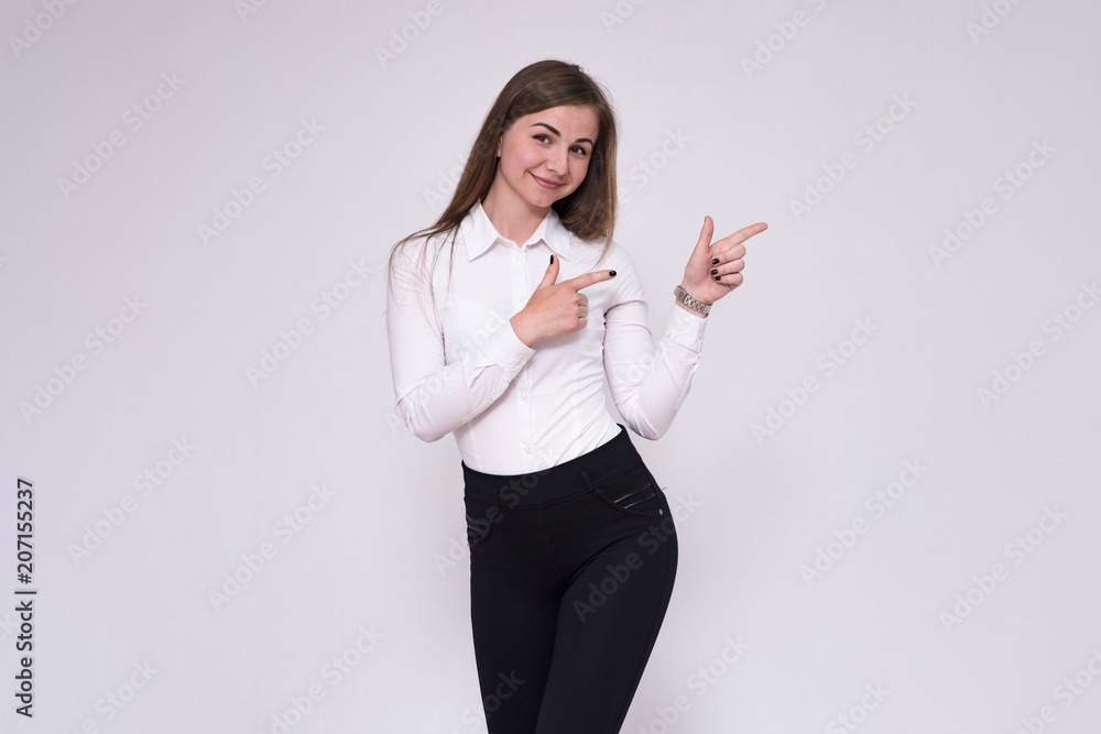 portrait of a beautiful brunette girl on a white background in a white shirt showing on a product. portrait of a beautiful brunette girl on a white background in a white shirt showing on a product.