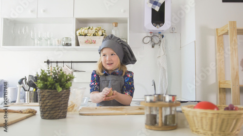 Little caucasian girl in apron rolls out the dough on the board