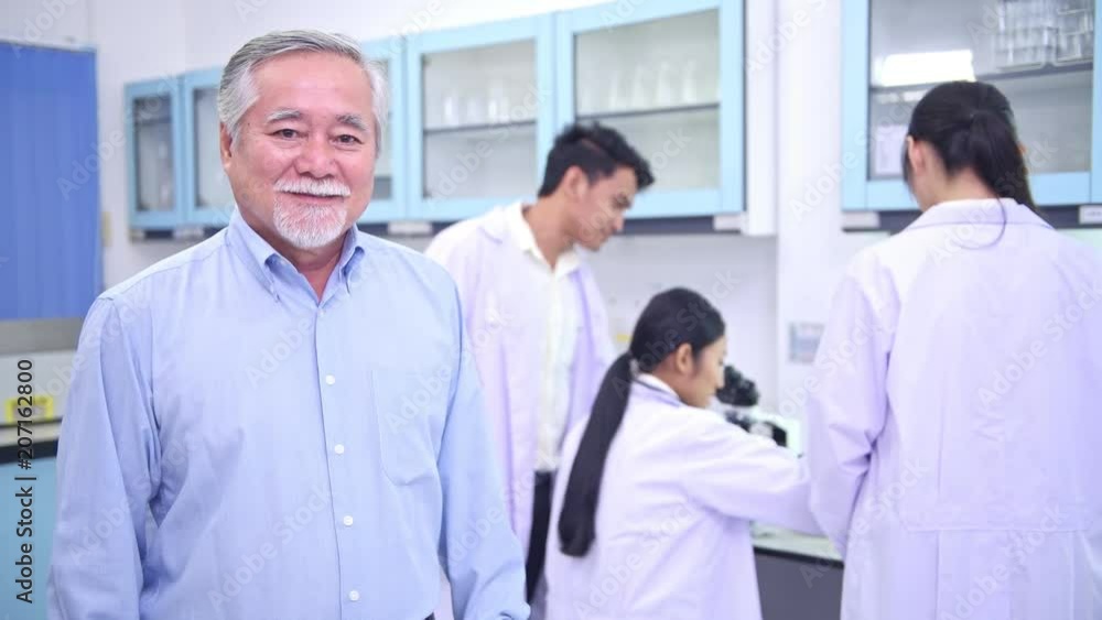 Scientists working in lab portrait. Senior chinese male scientist working in lab portrait with his team in background. Scientists working in lab portrait. Senior chinese male scientist working in lab portrait with his team in background.