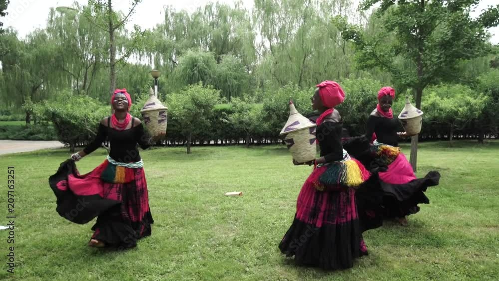 African women are dancing a folk traditional dance on a grass meadow, in traditional costumes with wicker baskets, sunny, trees' background, African costumes, traditions, African culture, tribes African women are dancing a folk traditional dance on a grass meadow, in traditional costumes with wicker baskets, sunny, trees' background, African costumes, traditions, African culture, tribes