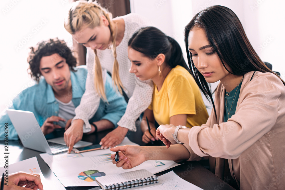 young asian businesswoman looking at wristwatch while her partners working behind at modern office young asian businesswoman looking at wristwatch while her partners working behind at modern office
