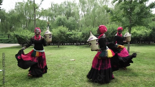 African women are dancing a folk traditional dance on a grass meadow, in traditional costumes with wicker baskets, sunny, trees' background, African costumes, traditions, African culture, tribes