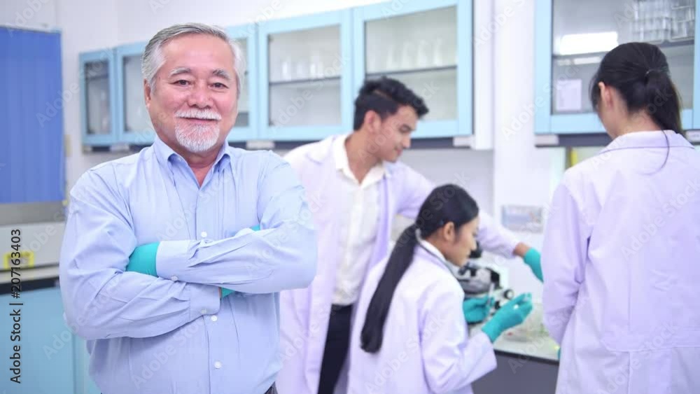 Scientists working in lab portrait. Senior chinese male scientist working in lab portrait with his team in background. Scientists working in lab portrait. Senior chinese male scientist working in lab portrait with his team in background.