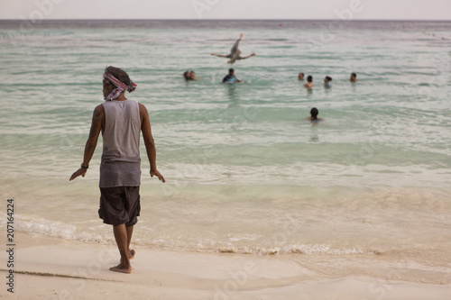 Islander walking on the beach, background of  group of friends playing and enjoying together photo