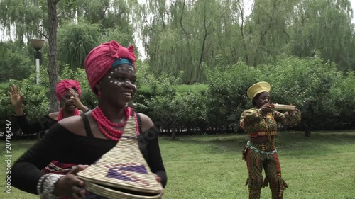 African women are dancing a folk traditional dance on a grass meadow, in traditional costumes with wicker baskets, sunny, trees' background, African costumes, traditions, African culture, tribes