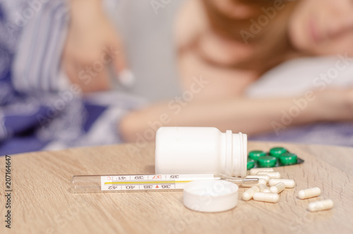 Woman lies in bed sick with thermometer jar of pills medicine flu virus temperature