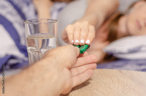 Woman lies in bed sick giving pills glass of water health care medical