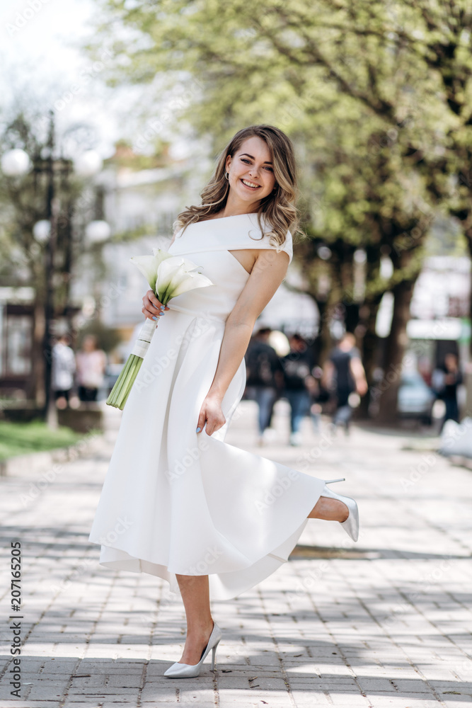 Naklejka premium The charming bride keeps a wedding bouquet and stands on the street