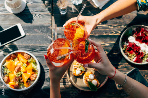 Overhead view of three women making a celebratory toast with aperol spritz cocktails