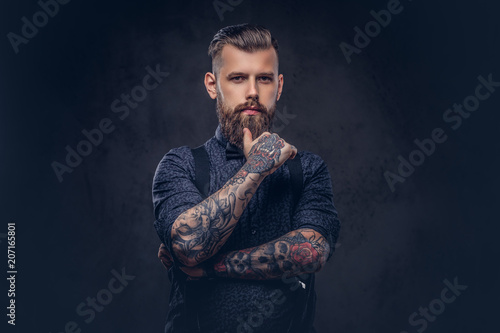 Pensive handsome old-fashioned hipster in a blue shirt and suspenders, standing with hand on chin in a studio. photo