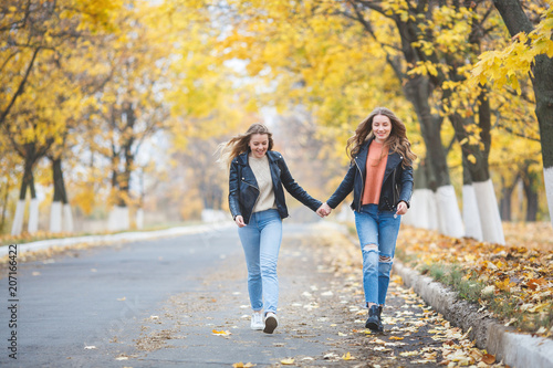 Young pretty girls having fun outdoors in autumn background. Cheerful friends in the fall time