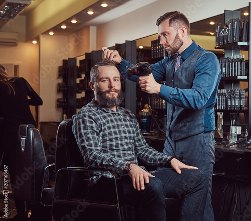 Professional barber working with a client in a hairdressing salon, uses a hair dryer.
