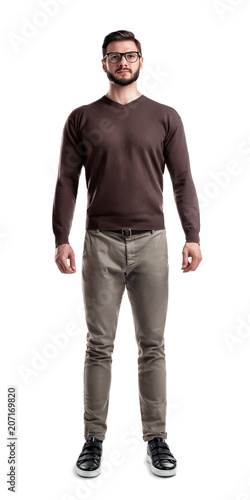 A young bearded man in casual wear stands with hands on his sides on a white background.