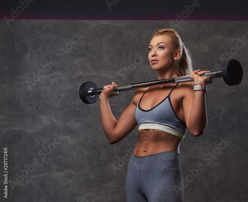 Beautifull fitness woman in gray sportswear doing exercise with a barbell in the fitness center.