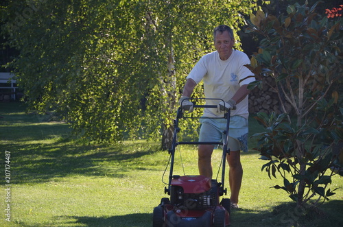 Homme senior passant la tondeuse dans son jardin.