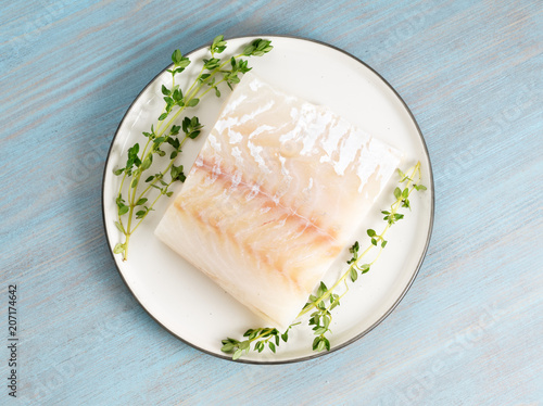 Canvas Print piece of raw cod fish fillet on plate on blue wooden table, top view