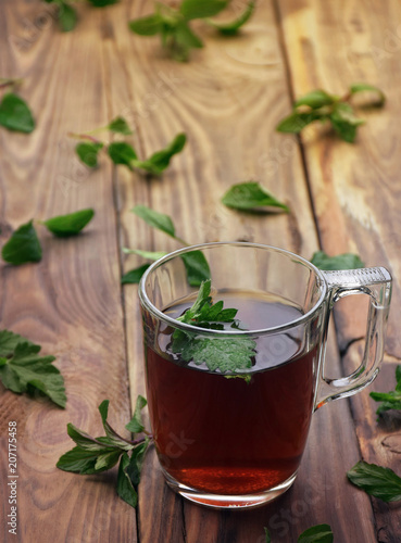 A fragrant herbal tea with mint leaves, lemon balm, raspberries and currants. Close-up. A cup of herbal tea on a wooden background.