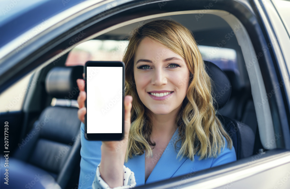 Young woman in auto shows smartphone with blank screen.