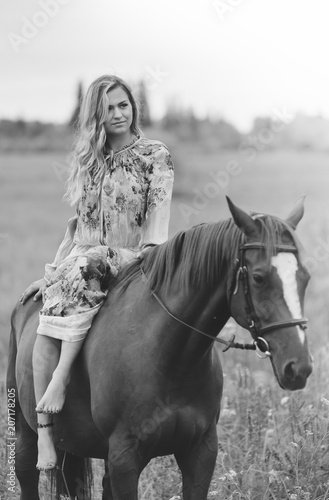 Young woman sits on a horse in a summer meadow © sergo321