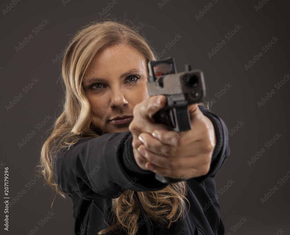 Woman in studio aiming in to shoot a gun. Woman in studio aiming in to shoot a gun.