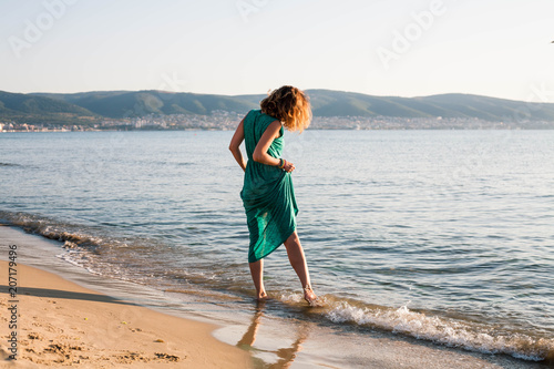 A young girl in a green dress is standing on the sea.