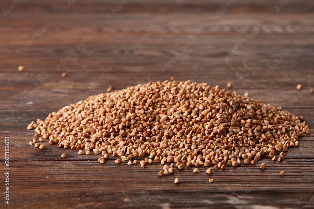 Obraz premium Pile of buckwheat groats on wooden background, top view, close-up, selective focus, shallow depth of field
