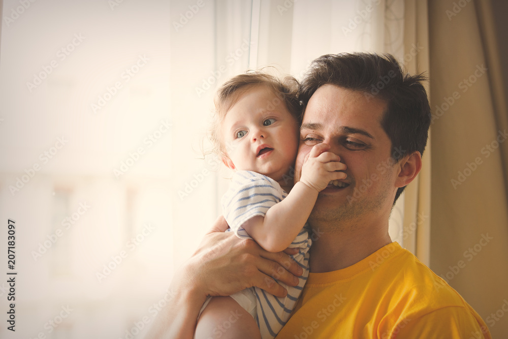 Young brunet father in yellow shirt playing with a little baby at home.