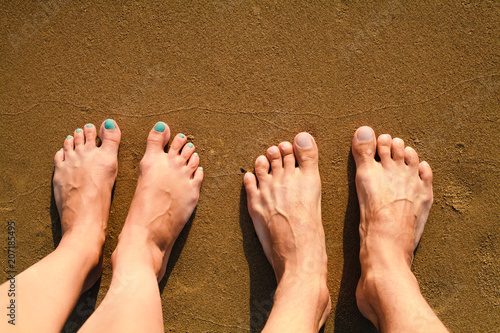 Male and female feet are standing on the sandy beach. © Markoff
