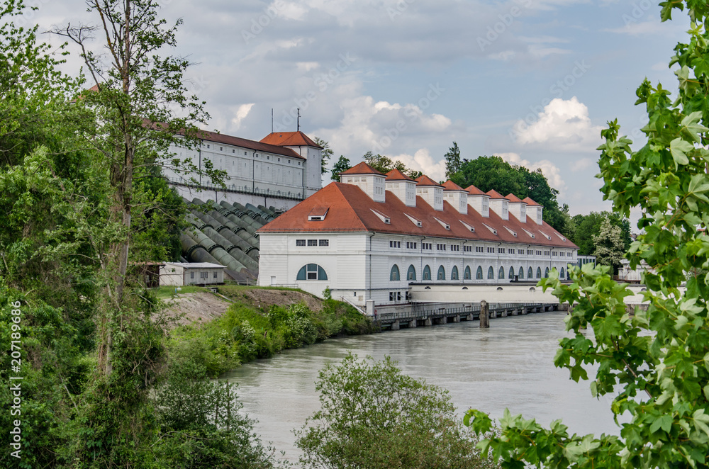 Obraz premium Old power station for energy generation on river bank with dam behind building