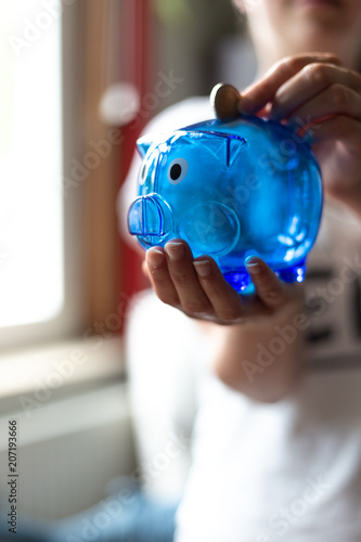 Junge Frau hält blaues Sparschwein in der Hand und wirft Geld hinein