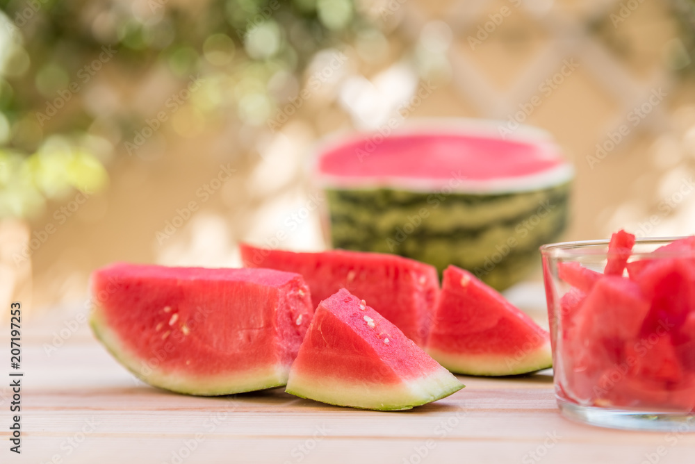 watermelon slices on wooden table and glass cup with pieces of watermelon, mediterranean garden background