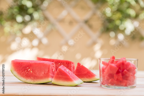 watermelon slices on wooden table and glass cup with pieces of watermelon, mediterranean garden background