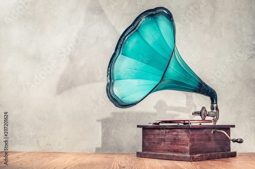 Vintage antique aged aquamarine gramophone phonograph turntable on wooden table front concrete wall background with its shadow. Retro old style filtered photo