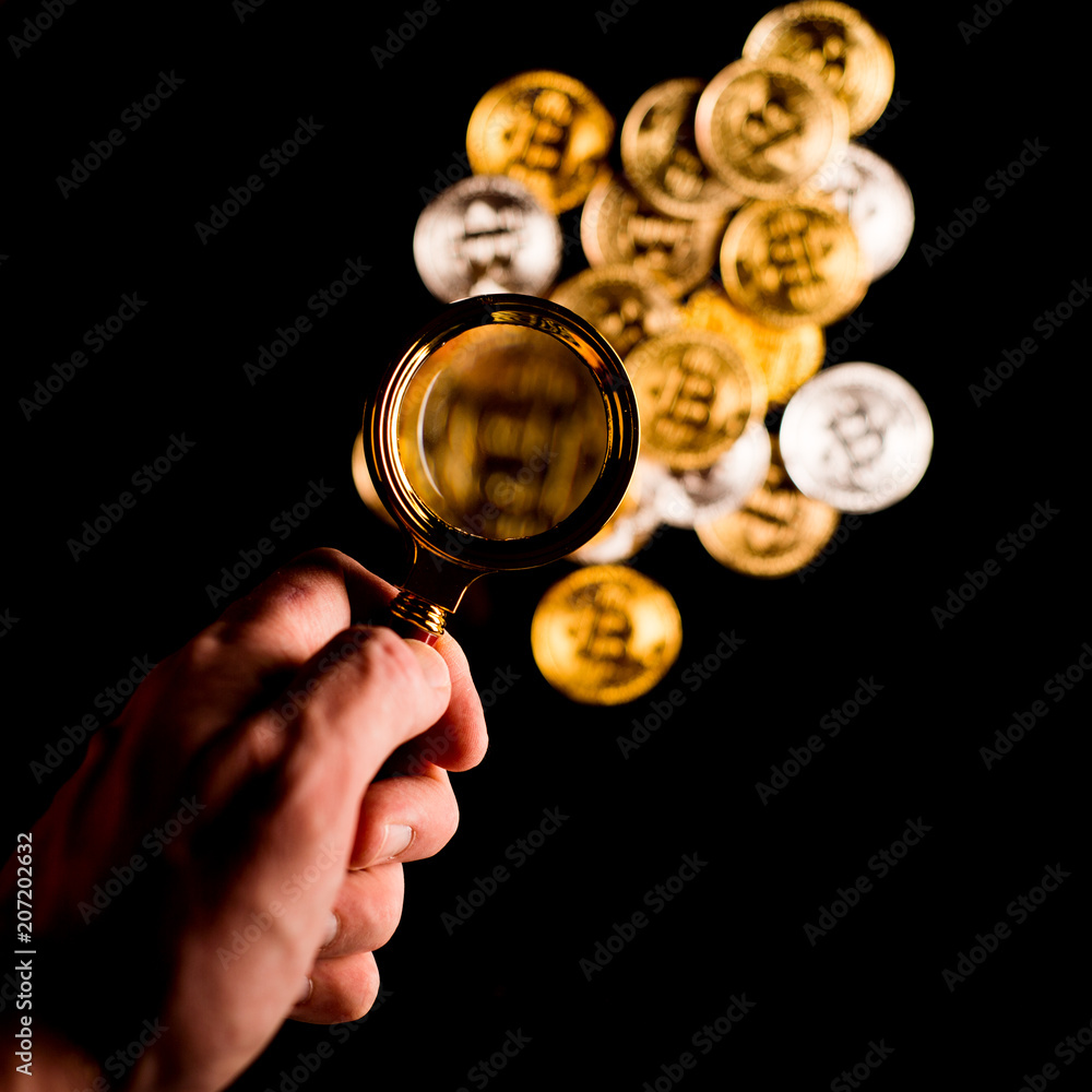 Person holding magnifying glass and looking through it on new virtual money golden bitcoin placed on a black background. Person holding magnifying glass and looking through it on new virtual money golden bitcoin placed on a black background.