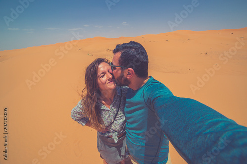 Happy tourist couple smiling take photo selfie in the Middle of the red Sahara desert with giant red dunes in background