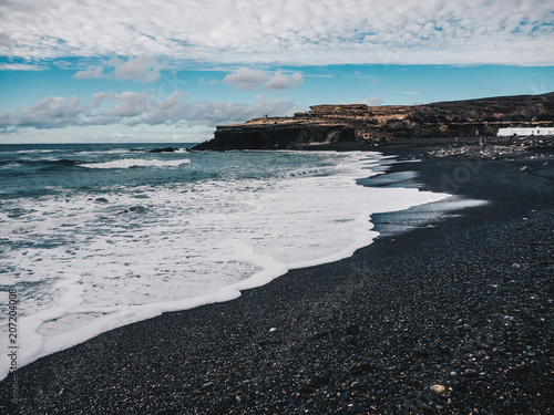 Stormy ocean waves with white foam hitting the black sand beach of Ajuy in Fuerteventura, Canary Islands, Spain.