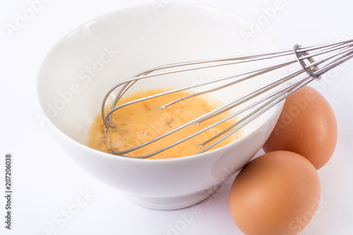 Whisking eggs in bowl. Preparing omelet with whisk and eggs on white desk in kitchen. Cooking and food concept. Close up, selective focus