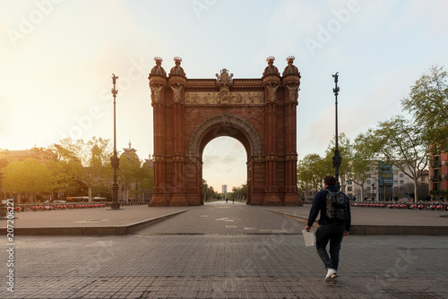 Tourist sightseeing Bacelona Arc de Triomf during sunrise in the city of Barcelona in Catalonia, Spain. The arch is built in reddish brickwork in the Neo-Mudejar style photo