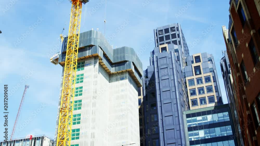 LONDON - MAY, 2017: Crane and modern buildings under construction against blue sky in the City of London LONDON - MAY, 2017: Crane and modern buildings under construction against blue sky in the City of London