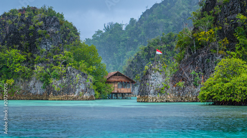 Bamboo Hut between some Rocks under Rain in Bay with Indonesian Flag, Pianemo Islands, Raja Ampat, West Papua, Indonesia
