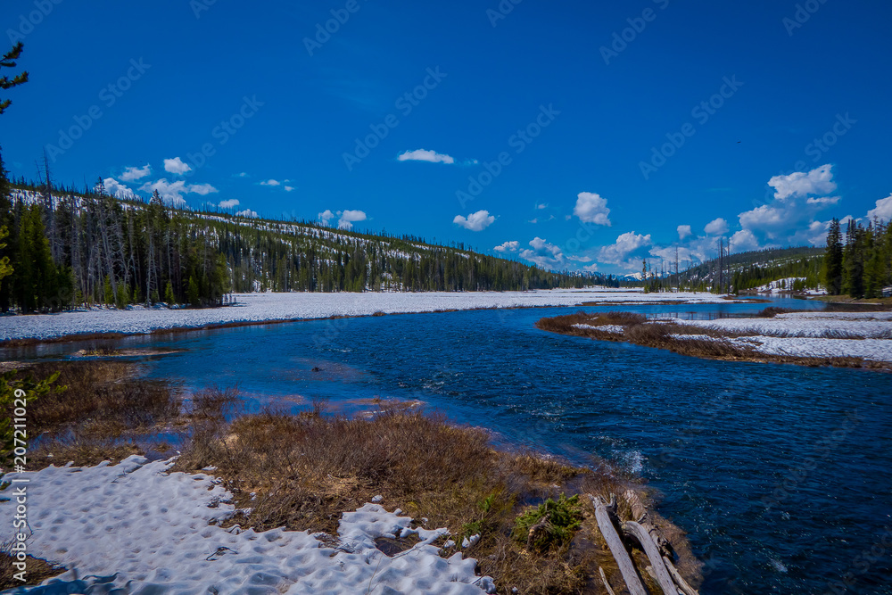 Outdoor view of partial frozen river in Yellowstone National Park with blue sky