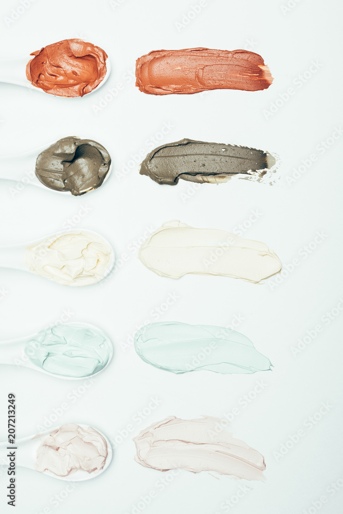 top view of spoons and various colorful clay mask smudges placed in row isolated on white surface top view of spoons and various colorful clay mask smudges placed in row isolated on white surface