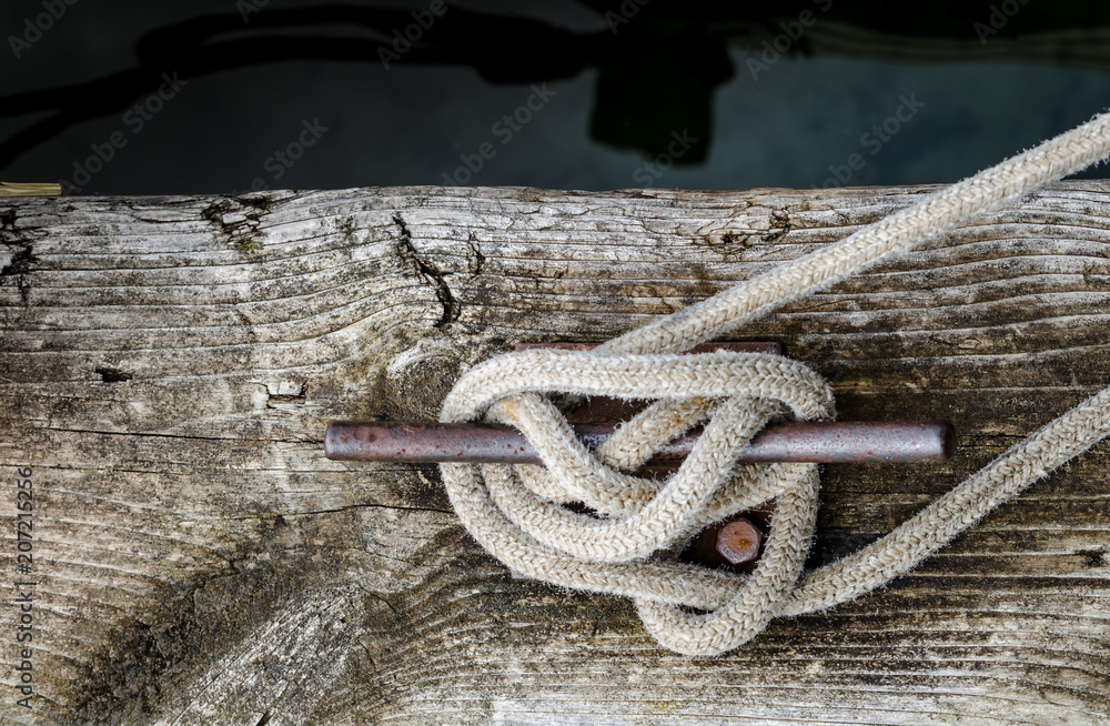 A weathered and grainy old dock board with an old rope tied to a rusty cleat