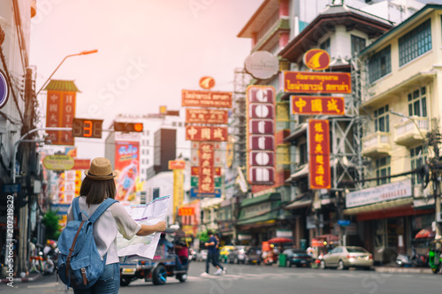 Young asian woman traveler with blue backpack and hipster hat looking map on road with tuk tuk Thailand background at China Town Bangkok. Traveling in Bangkok Thailand photo