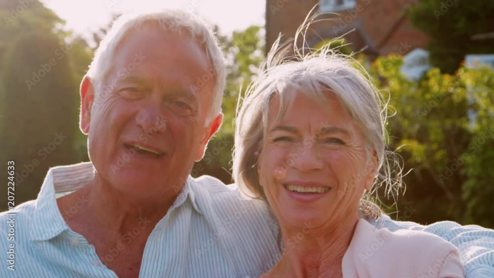 Portrait Of Senior Couple Sitting On Garden Bench In Evening Portrait Of Senior Couple Sitting On Garden Bench In Evening