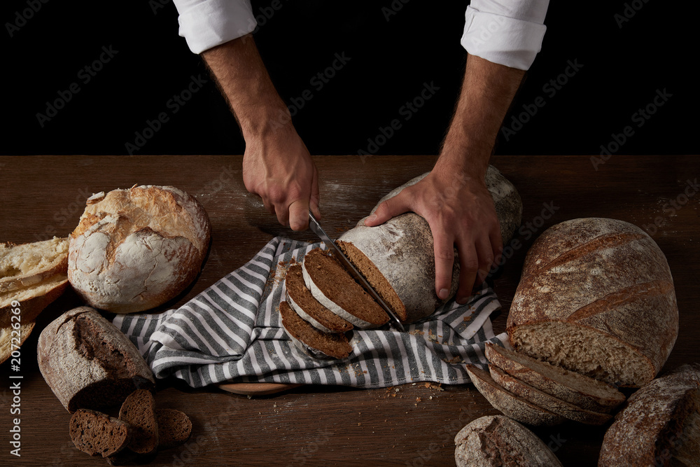cropped image of male baker cutting bread by knife on sackcloth on wooden table
