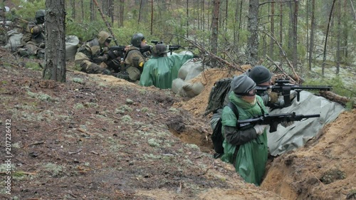 Soldiers in camouflage with combat weapons are being fired in the shelter of the forest, the military concept photo