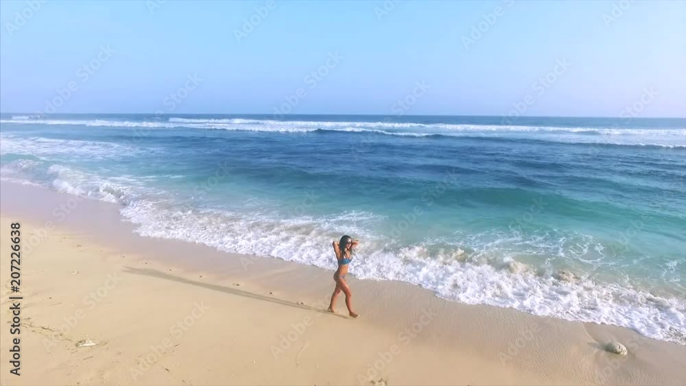 Sexual brunette woman walking and running along the ocean waves on tropical beach and straightening her hair. Aerial top view. Niang Niang beach. Bali, Indonesia Sexual brunette woman walking and running along the ocean waves on tropical beach and straightening her hair. Aerial top view. Niang Niang beach. Bali, Indonesia