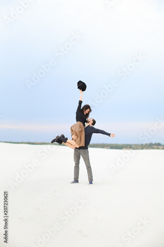 Young european man picking up on hands woman wearing skirt in white snow background. Concept of romantinc winter photo session. photo