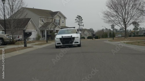 A police squad car drives through a suburban neighborhood while on patrol.